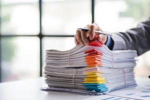 stack of paperwork with hand holding a pen