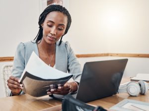 woman sitting at desk looking at paper with a laptop